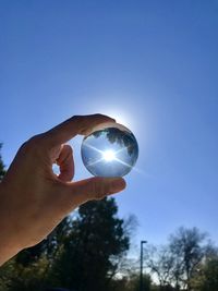 Person hand holding crystal ball against blue sky