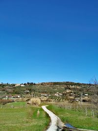 Road amidst field against clear blue sky