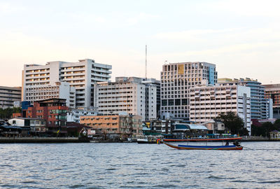 Buildings by river against sky in city