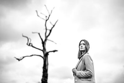 Woman standing by bare tree against sky
