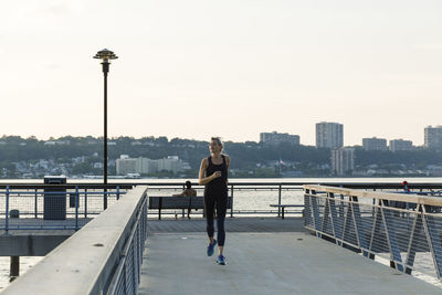 Woman jogging while exercising on bridge against clear sky in city