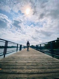 Skateboarder in front of cloudy sky standing on footbridge