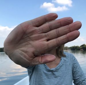 Close-up of woman showing stop gesture while sitting on boat on lake against sky