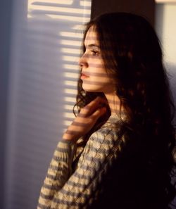 Sunlight falling on young woman standing by wall