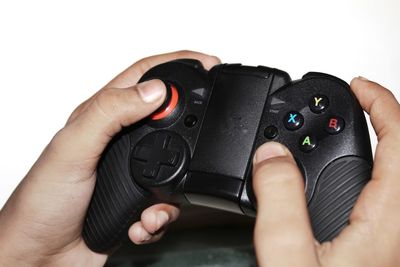 Close-up of hand holding game controller over white background