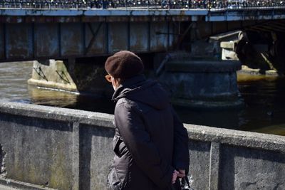 Rear view of man with hands behind back walking on bridge