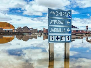 Information sign by lake against sky in city