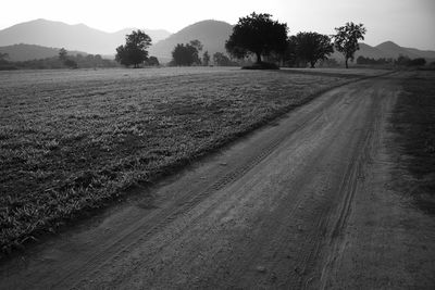 Dirt road amidst field against sky