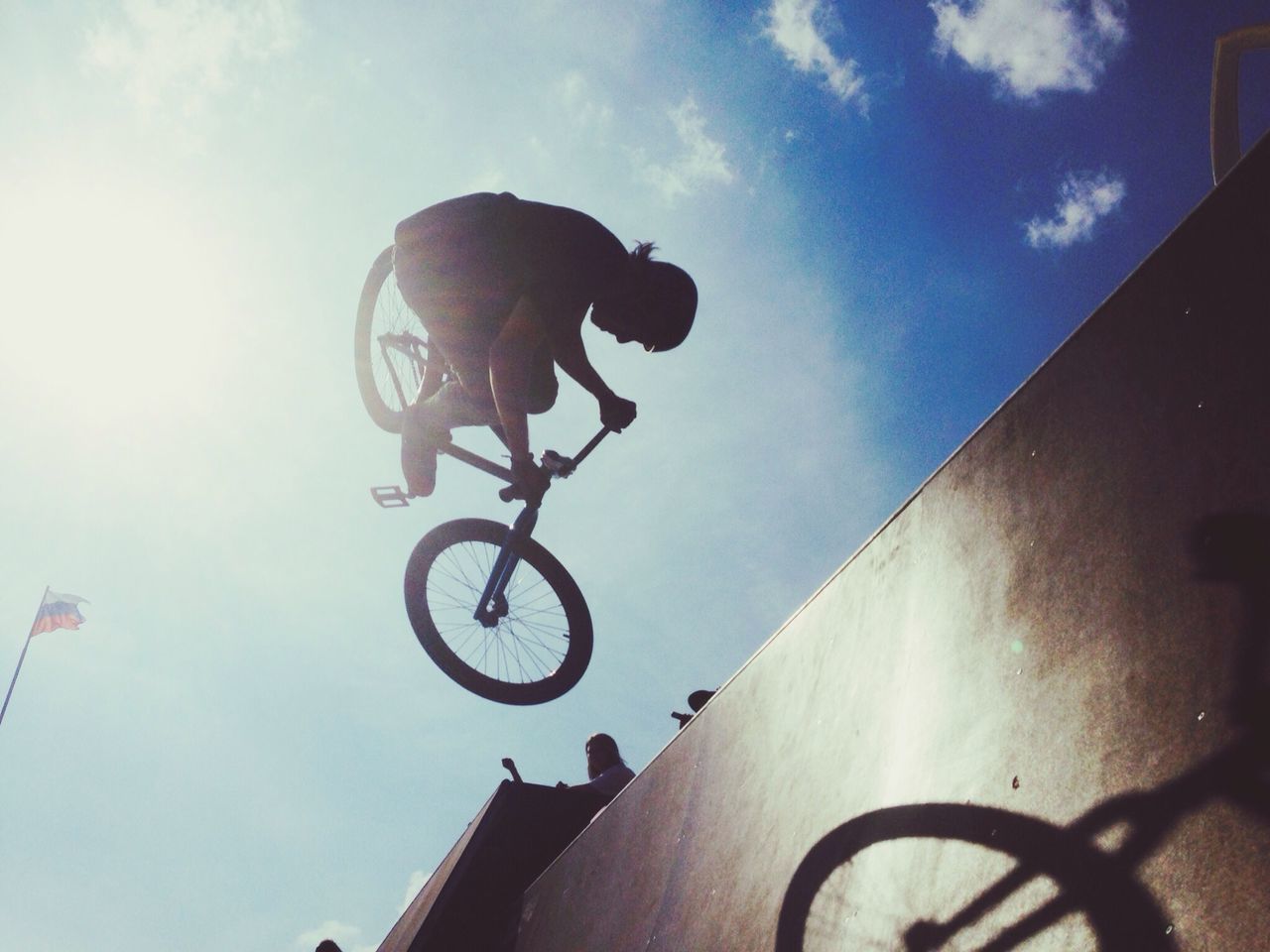 low angle view, bicycle, sky, built structure, architecture, cloud - sky, building exterior, transportation, street light, mode of transport, silhouette, day, land vehicle, cloud, outdoors, lighting equipment, sunlight, men