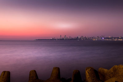 Scenic view of sea by illuminated buildings against sky at sunset