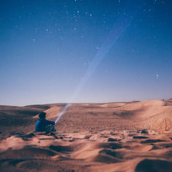 Man with flashlight sitting on sand at desert against star field