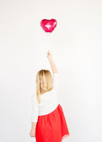 Back view little blond girl in red tutu holding red heart balloon