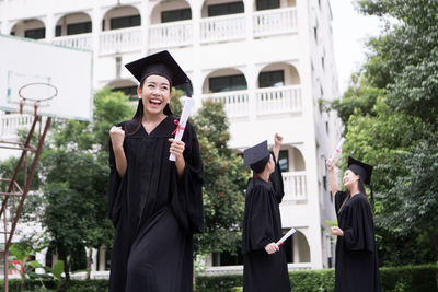 Cheerful student with clenched fist wearing graduation gown