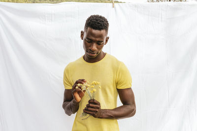 African american male with bouquet of yellow wildflowers looking down on white background