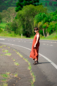 Young woman wearing sunglasses standing on road against trees in forest