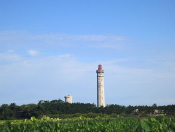 Lighthouse on field by building against sky