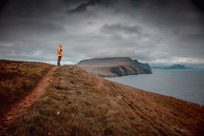 Full length of man standing on cliff by sea against sky