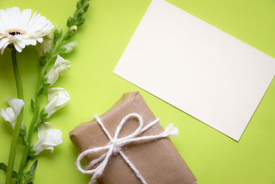 Close-up of flowers with paper and gift box against green background