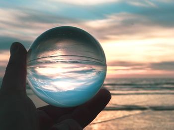 Close-up of hand holding crystal ball against sunset sky