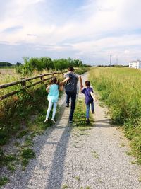 Rear view of man and children running on footpath against cloudy sky