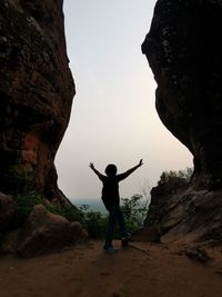 Rear view of man standing on rock against sky