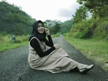 Young woman using phone while sitting on land