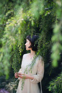 Young woman looking away while standing on tree