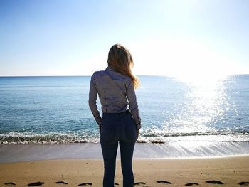 Rear view of woman standing on sea shore at beach against clear sky