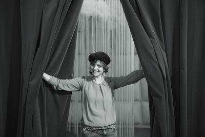 Portrait of young woman smiling while standing amidst curtains