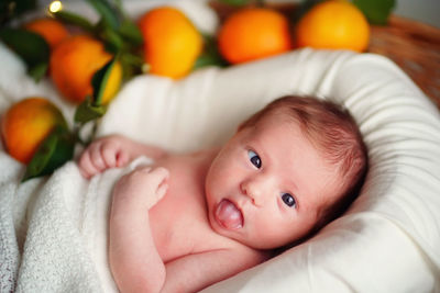 Caucasian newborn cross-eyed baby lies in a basket of tangerines under a white blanket.