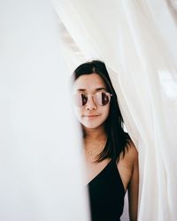 Portrait of young woman standing against white curtain