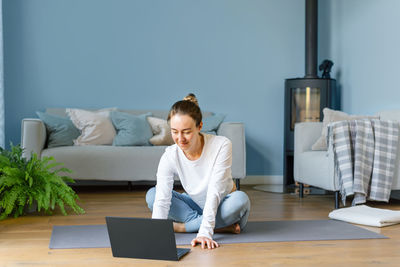 Young woman using laptop while sitting on bed at home