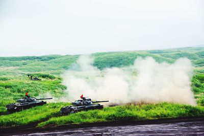 Armored tanks firing on grassy field against sky