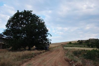 Dirt road amidst field against sky