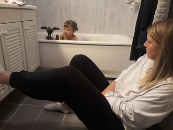 Woman looking at boy playing with toys in bathtub at home