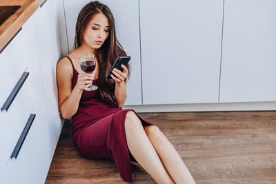 Young woman using mobile phone while sitting on wall