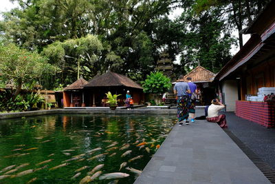 People on house by canal amidst trees during rainy season