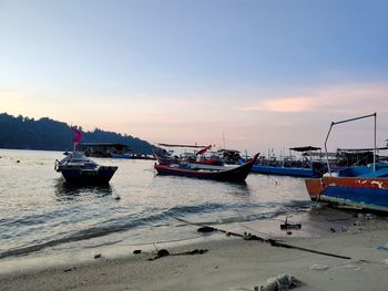 Boats moored on sea against sky during sunset