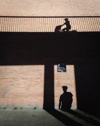 Silhouette man standing by brick wall