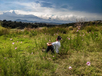 Full length side view of man sitting amidst pink flowers against sky