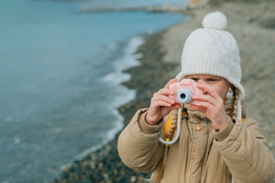 A little girl squinting photographs the autumn seascape on a childrens pink camera. the child