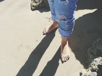 Low section of woman wearing torn jeans while standing at beach