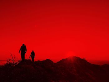 Silhouette men standing on mountain against orange sky