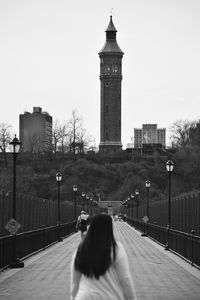 Rear view of people walking on high bridge with water tower in background