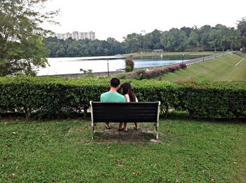 Rear view of man sitting on bench by lake