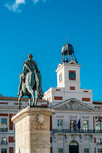 Low angle view of statue against building against clear blue sky