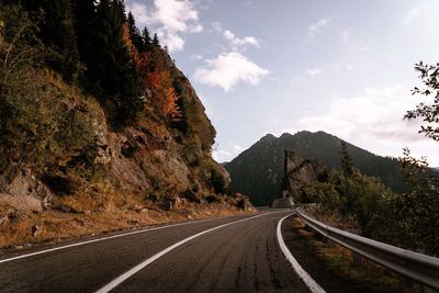 Empty road along trees and mountains against sky