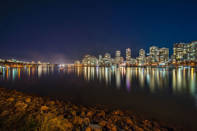 Illuminated city by sea against sky at night