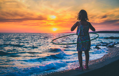 Rear view of child standing on beach during sunset