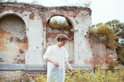 Young man looking at plants while standing against built structure